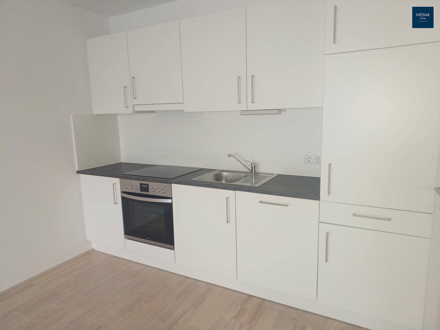 Neue, moderne Einbauküche mit weißen Schränken, dunkler Arbeitsplatte und integrierten Geräten.