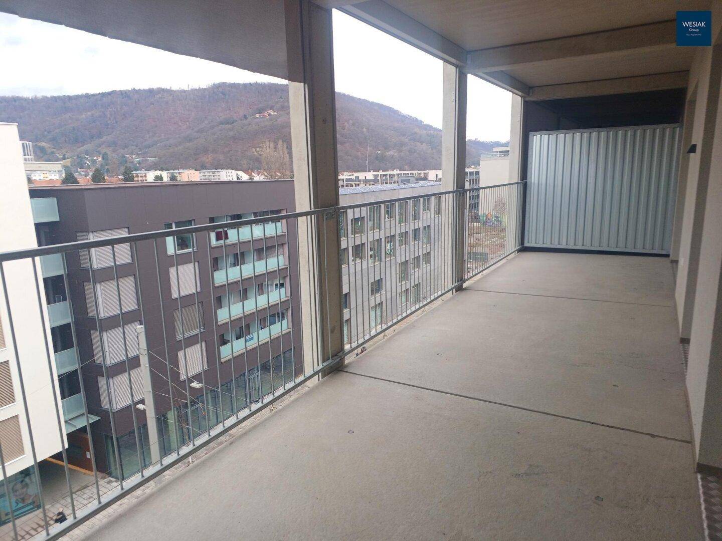 Langer Betonbalkon mit Metallgeländer und weitem Blick über die städtische Umgebung und Berge.