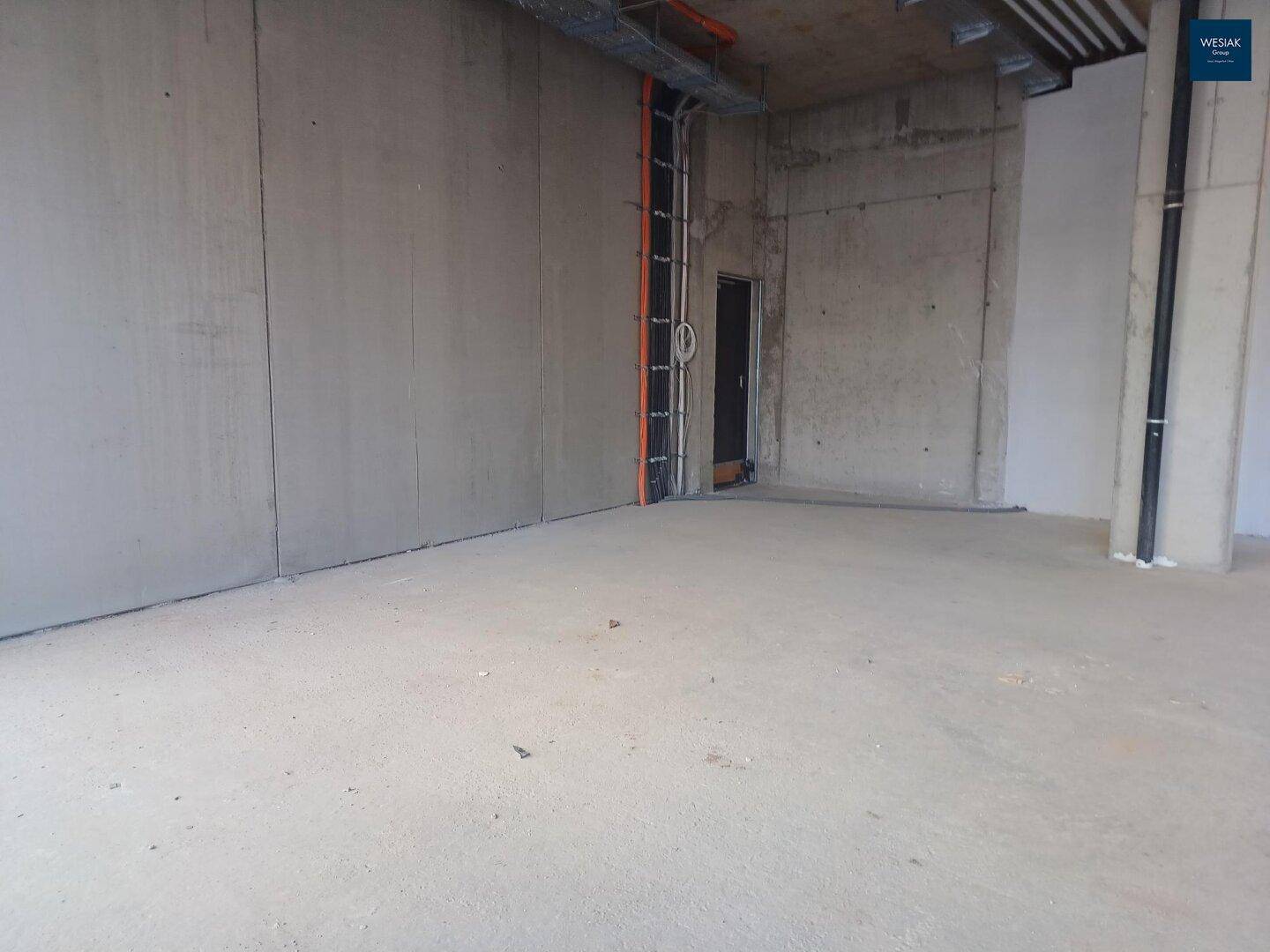 Unfertiger Innenraum eines Gewerbeobjekts mit Betonwänden und -boden, bereit für den Ausbau.