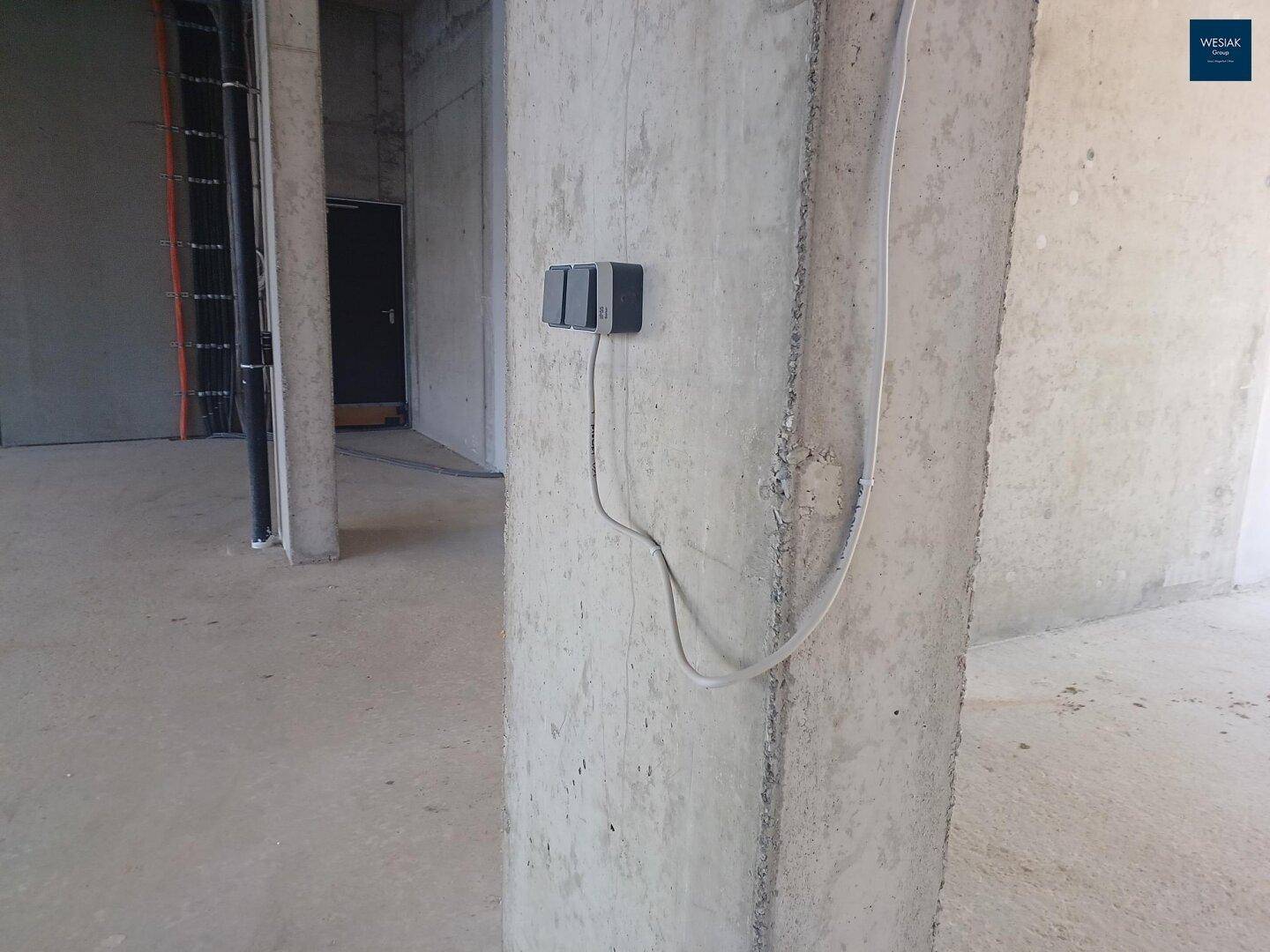 Detailansicht einer Betonsäule mit elektrischen Anschlüssen in einem unfertigen Gewerberaum.