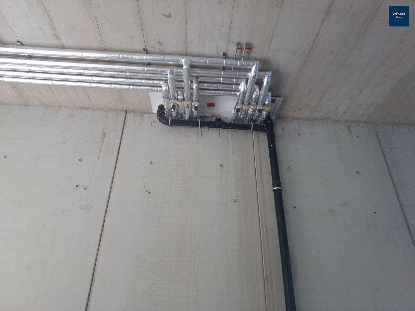 Deckeninstallationen mit isolierten Rohren und Leitungen in einem Rohbau-Gewerbebereich.