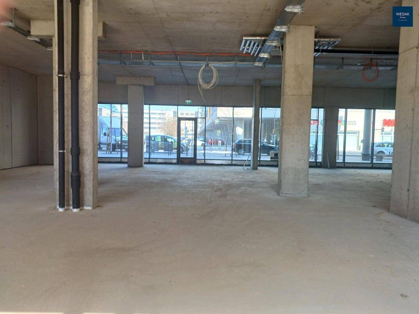 Geräumiger Gewerberaum mit mehreren Betonsäulen und großen Fensterfronten zur Straße hin.