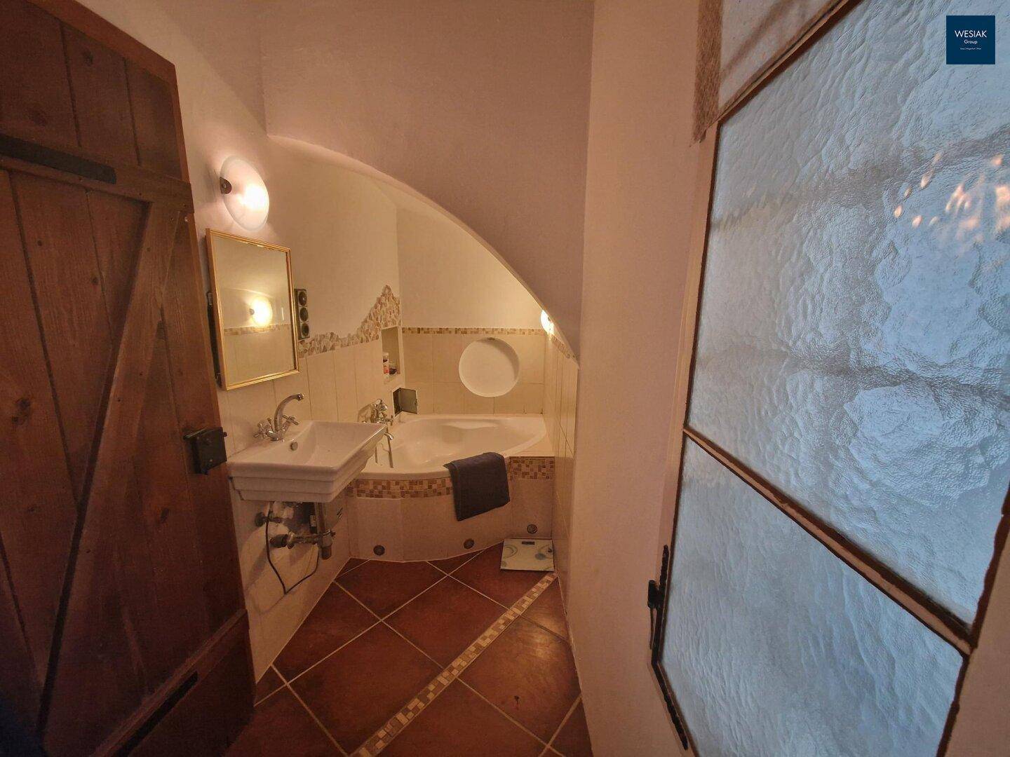 Badezimmer mit Badewanne, Waschbecken und Fliesenboden unter einer Dachschräge.