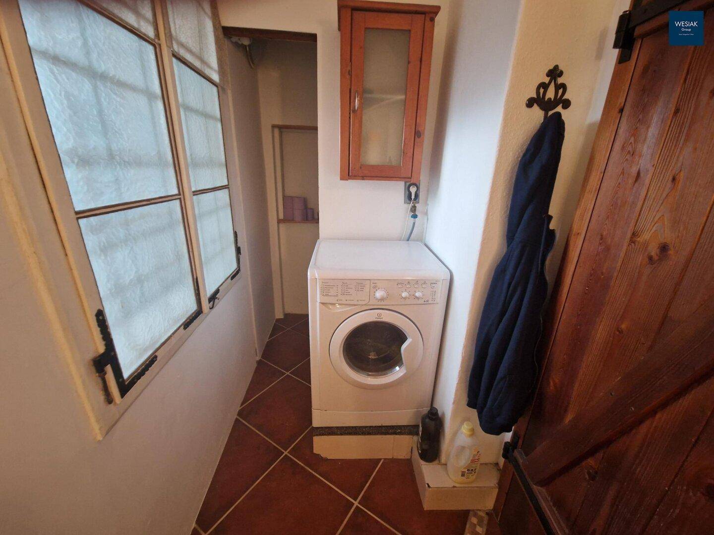 Kleiner Hauswirtschaftsraum mit Waschmaschine, Fliesenboden und Fenster.