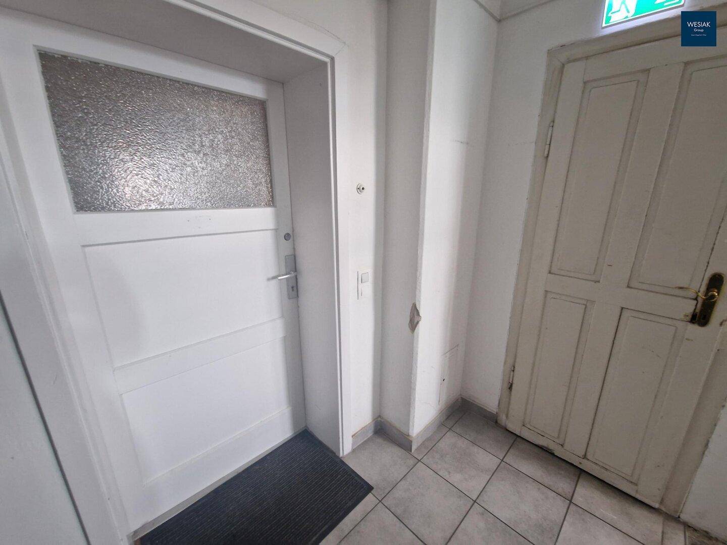 Eingangsbereich mit zwei Türen und Fliesenboden in einem Mehrfamilienhaus.