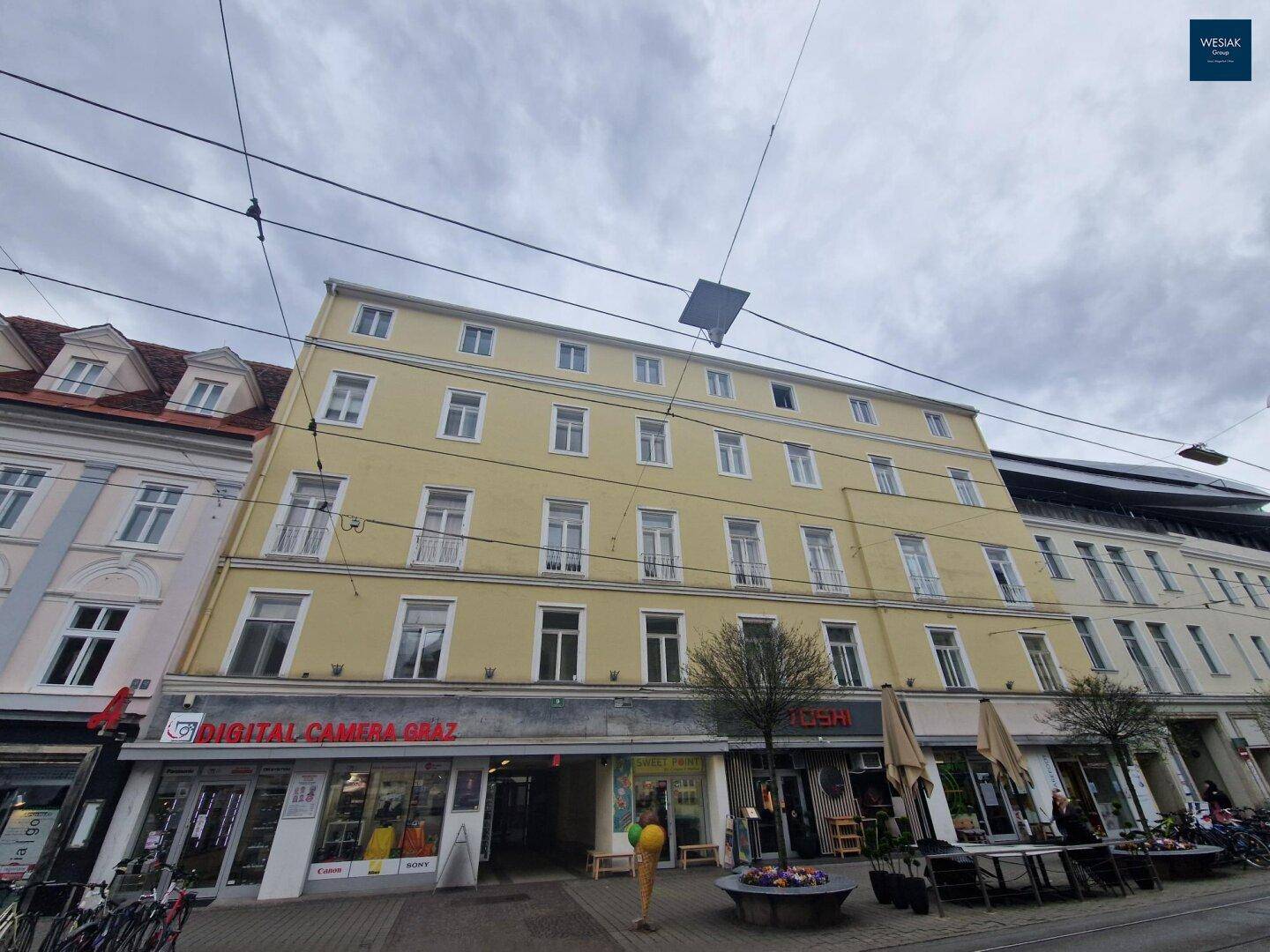 Historisches Gebäude mit gelber Fassade und Geschäften im Erdgeschoss in der Stadt.