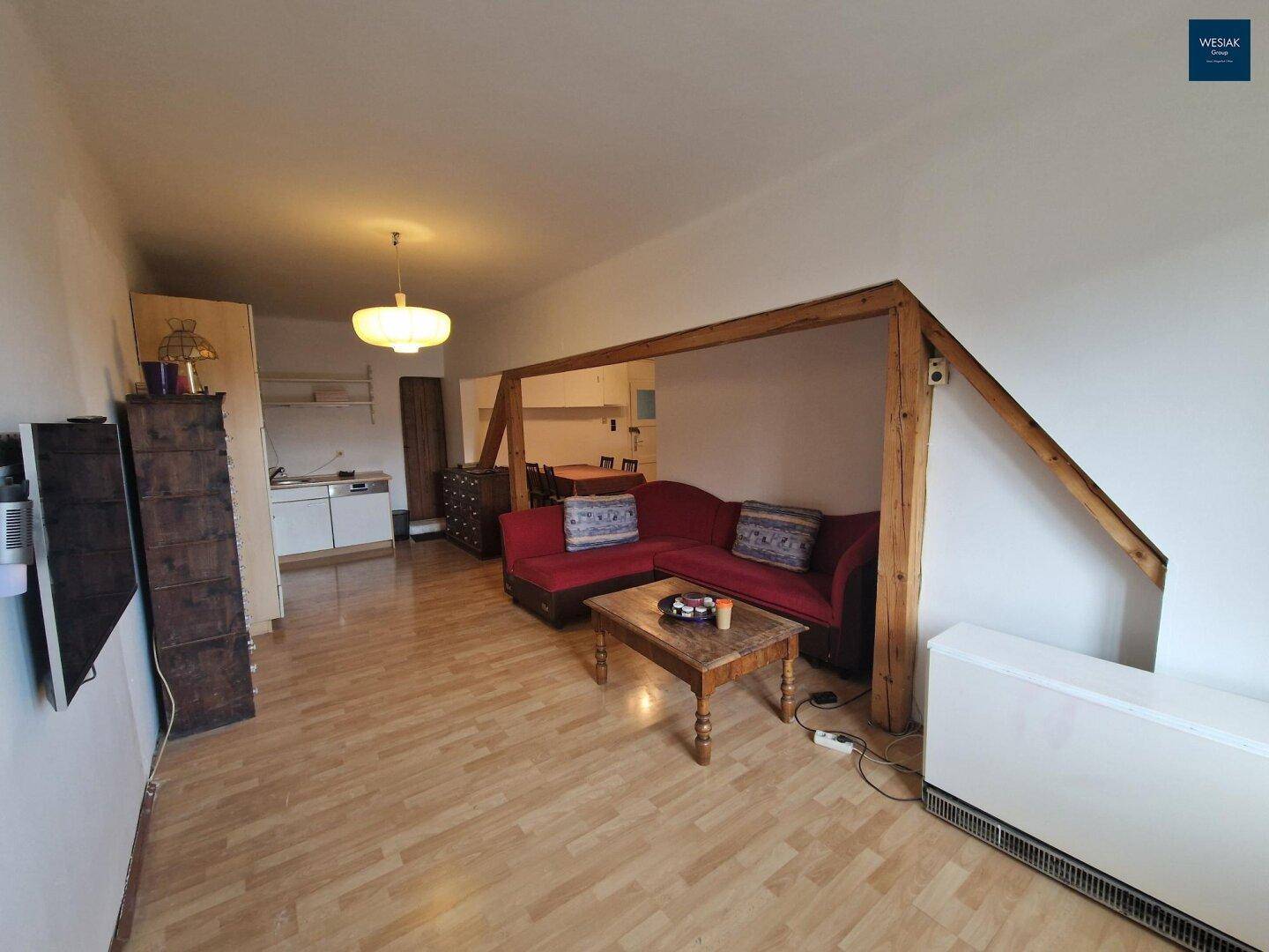 Offener Wohnbereich mit Holzbalken, Sofa und Blick auf den Essbereich und die Küche.