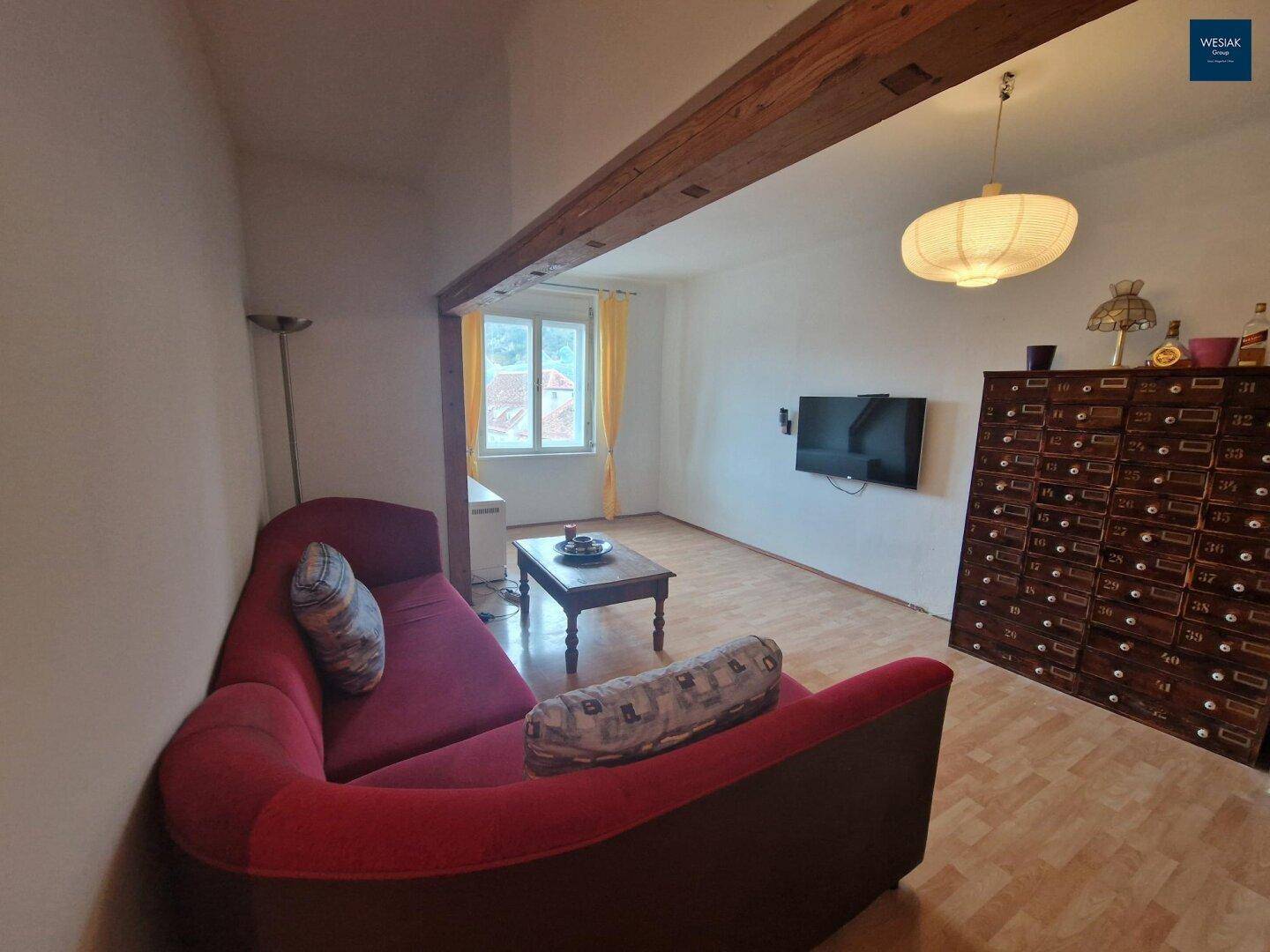 Gemütliches Wohnzimmer mit rotem Sofa, Holzbalken und Fenster mit Blick nach draußen.