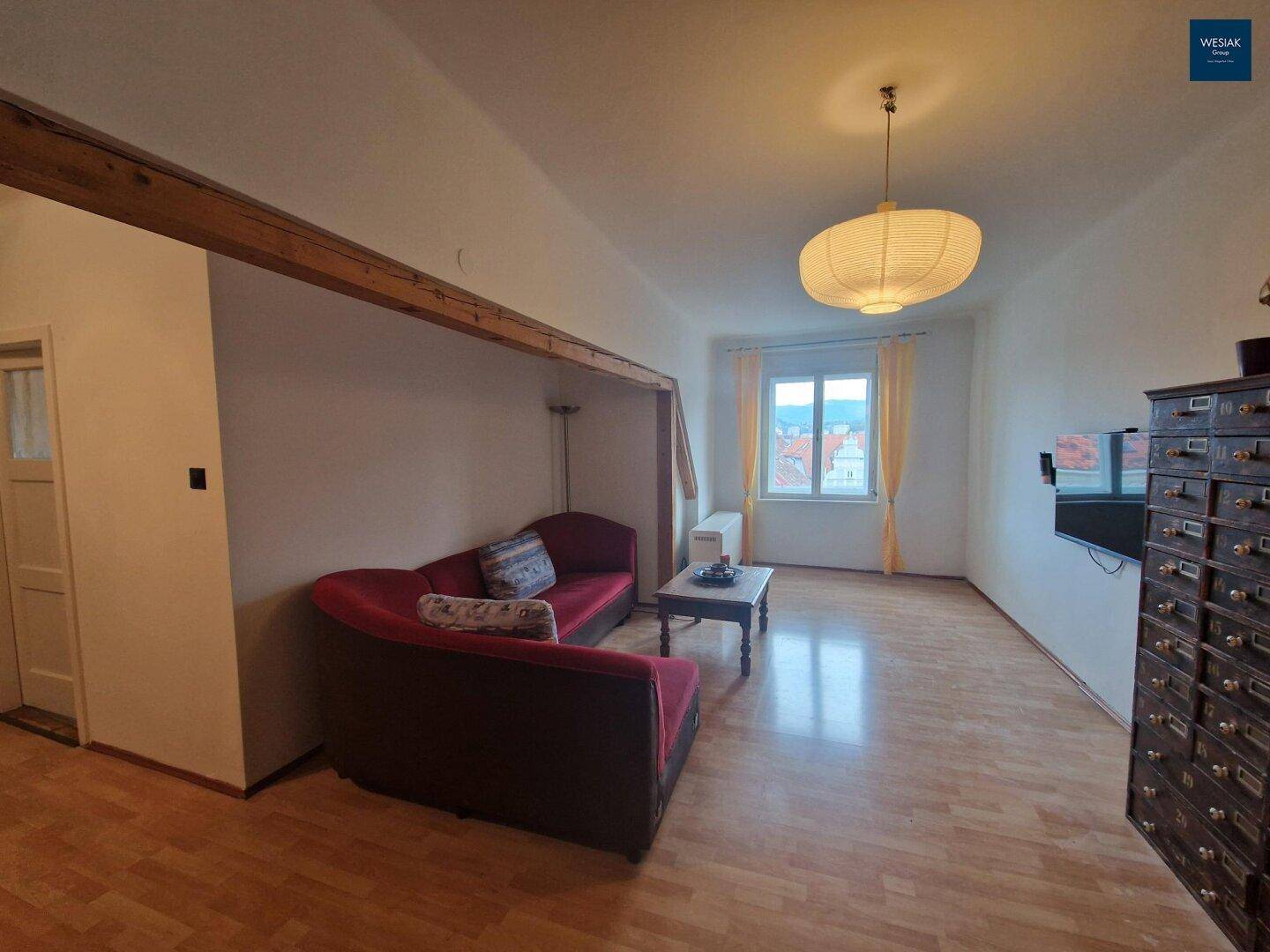 Geräumiges Wohnzimmer mit Holzboden, rotem Sofa und Fenster mit Stadtblick.