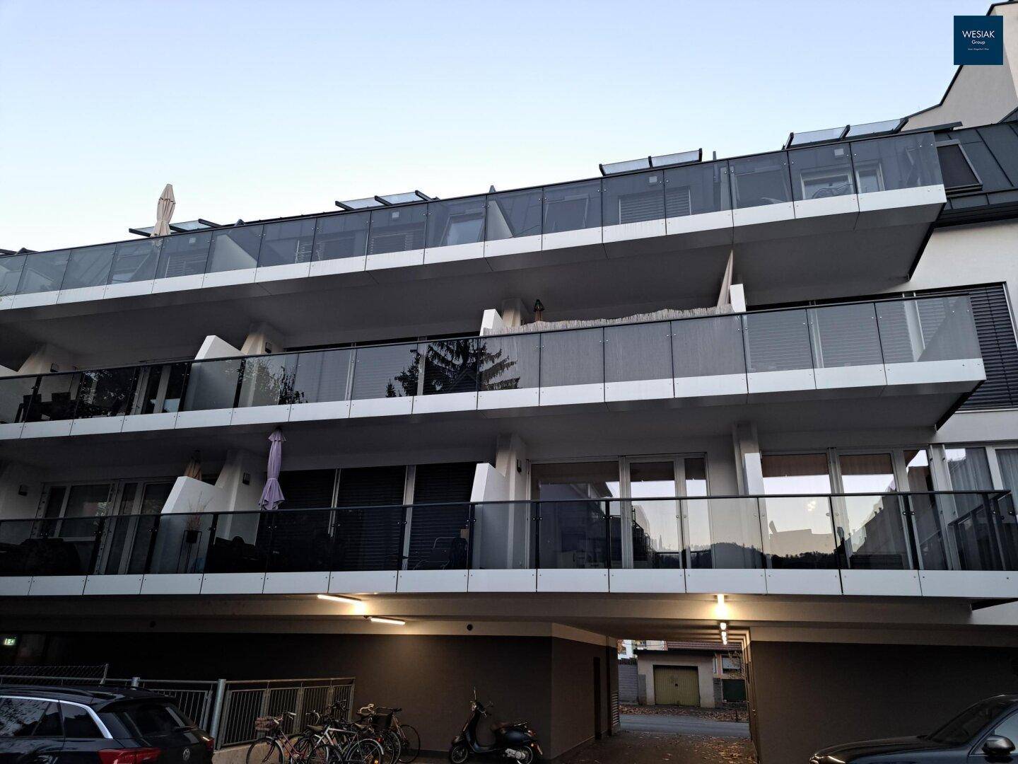 Moderne Gebäudefassade mit Glasbalkonen und Dachfenstern in der Dämmerung.