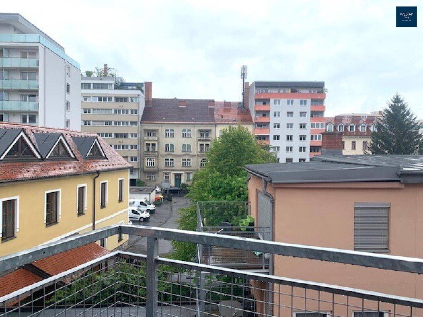 Blick über die Dächer der Stadt mit umliegenden Gebäuden und Bäumen unter bewölktem Himmel.