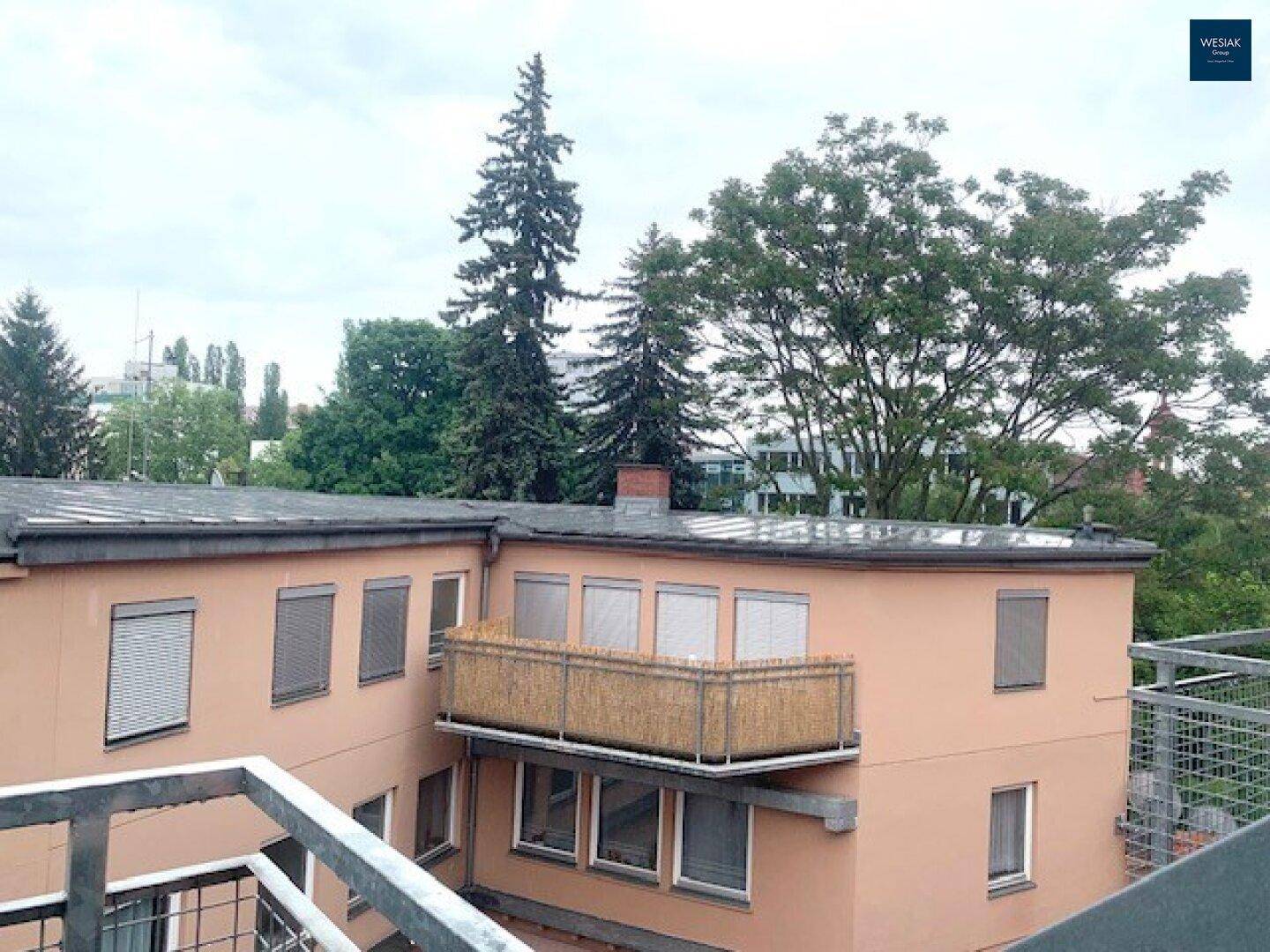 Blick auf ein Nachbargebäude mit kleinem Balkon und viel Grün in der Umgebung.