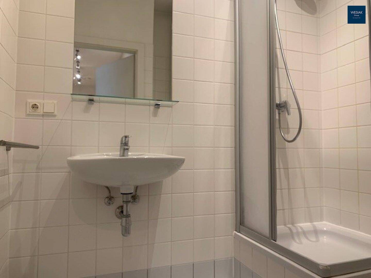 Gefliestes Badezimmer mit Dusche, Waschbecken, Spiegel und weißen Fliesen.