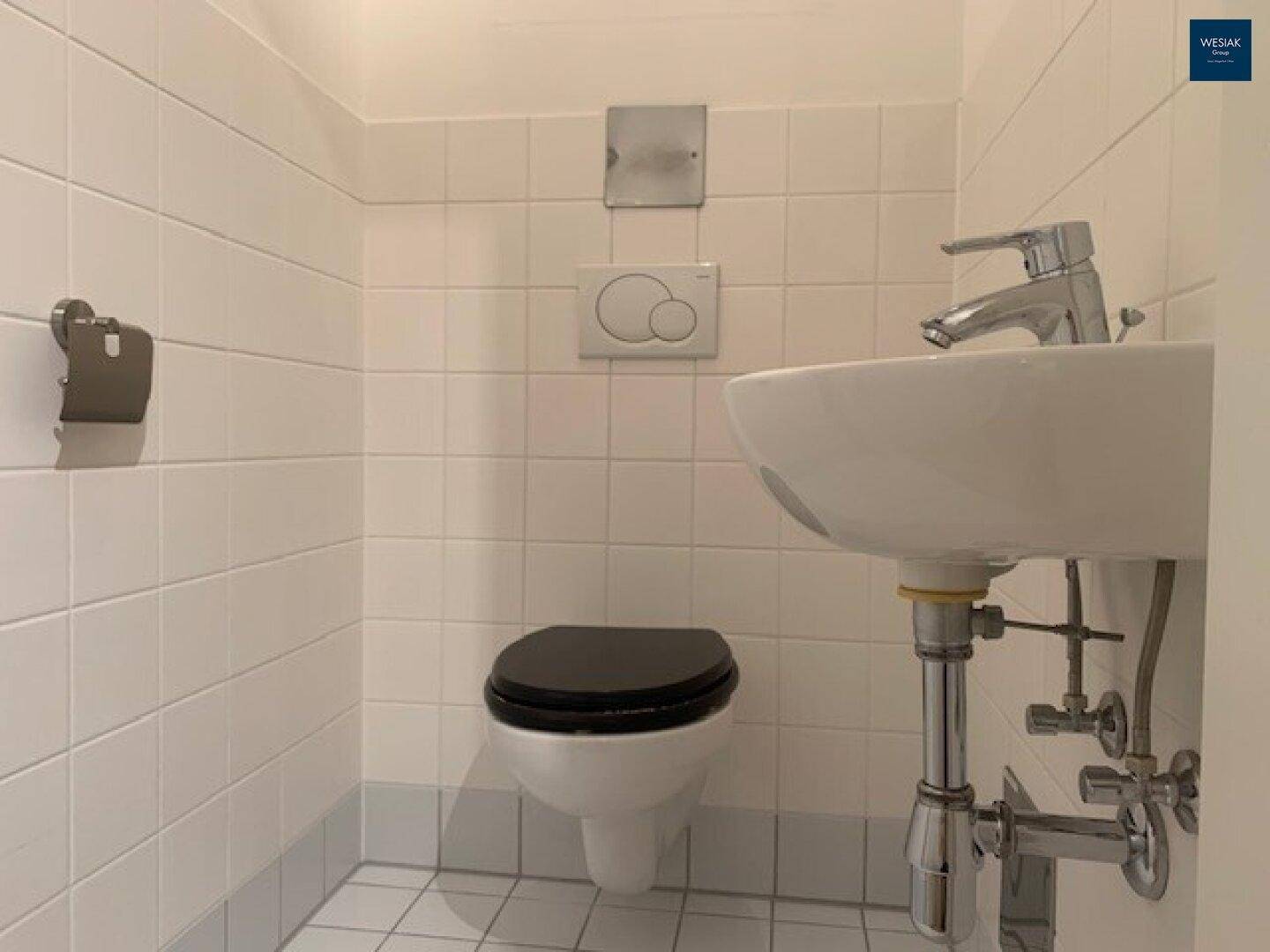 Separates WC mit Wand-WC, Waschbecken und weißen Fliesen.