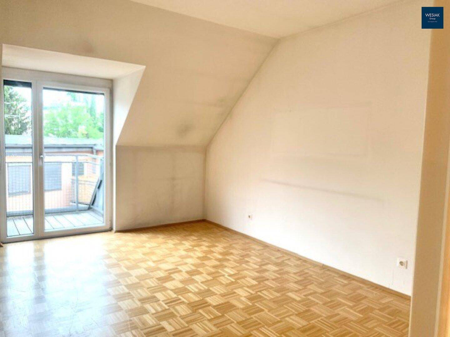 Lichtdurchflutetes Zimmer mit Dachschräge, Parkettboden und direktem Balkonzugang.
