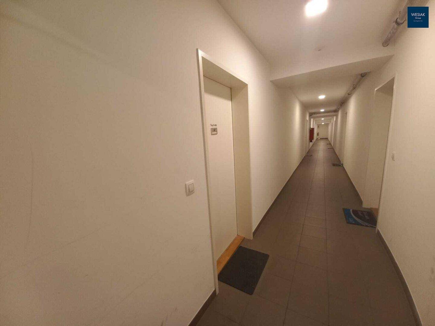 Langer, schmaler Flur mit Fliesenboden und mehreren Türen zu den Wohneinheiten.