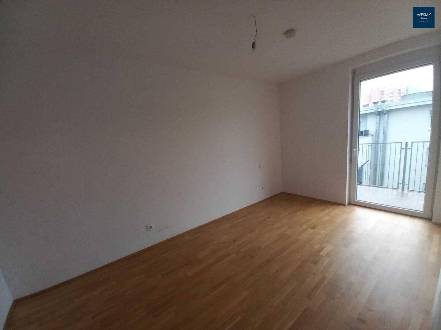 Geräumiger Raum mit hellem Parkettboden und großer Balkontür, ideal für individuelle Gestaltung.