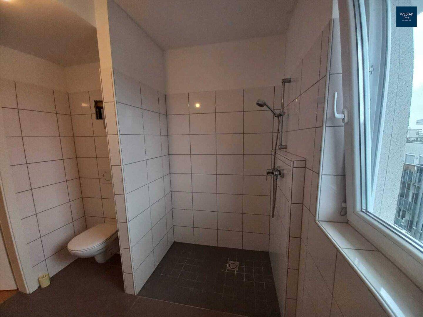 Modernes Badezimmer mit Duschbereich, WC und weißen Wandfliesen, in gutem Zustand.