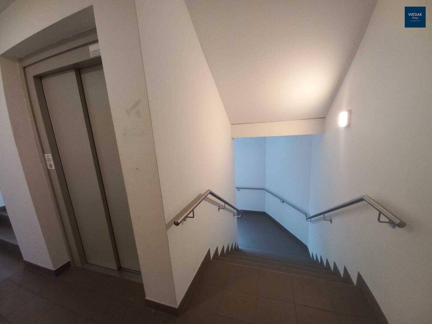 Treppenhaus mit Aufzug und Handläufen, gut beleuchtet und funktional gestaltet.