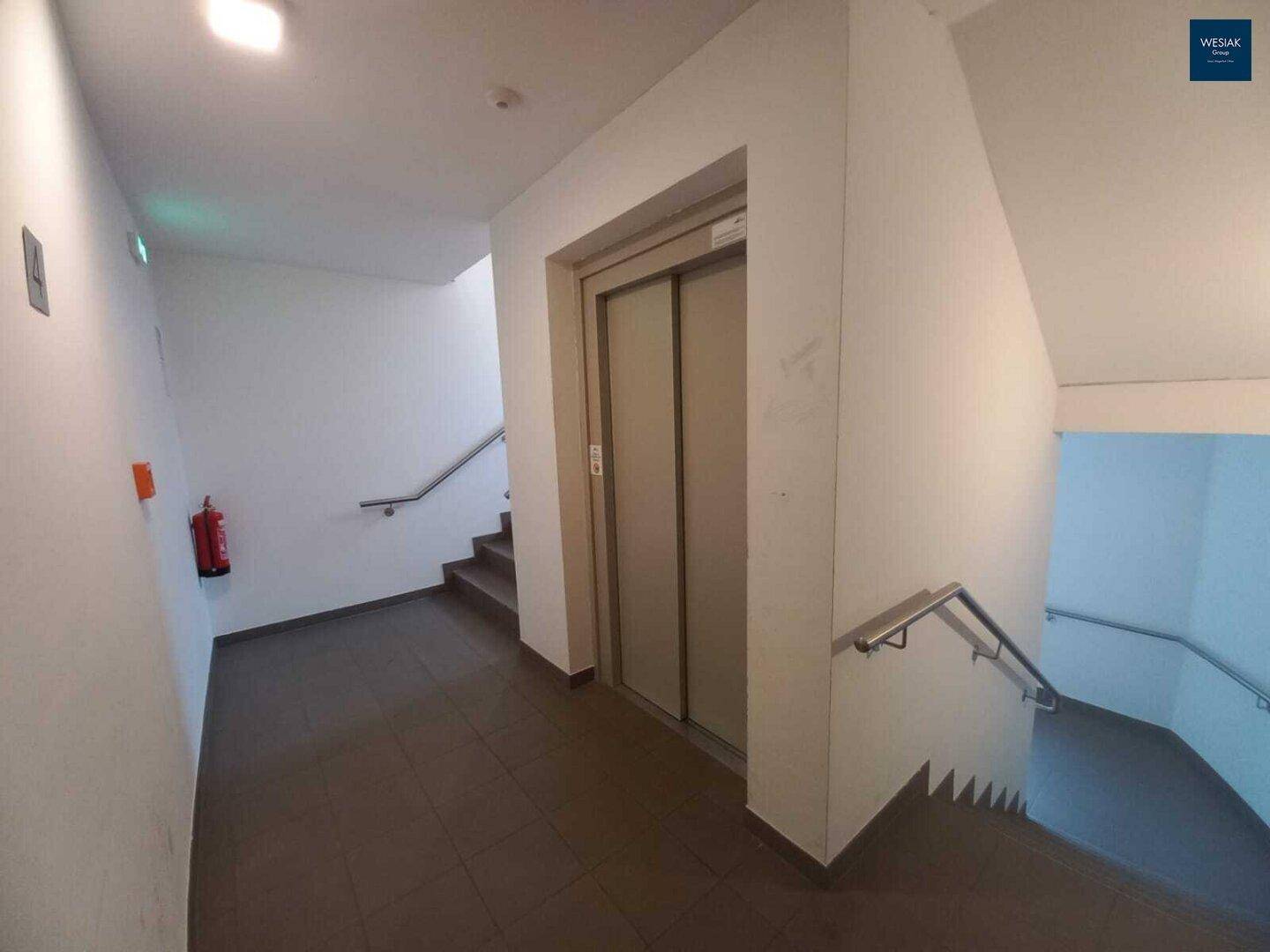 Heller Treppenhausbereich mit Aufzug und Fliesenboden in einem modernen Gebäude.