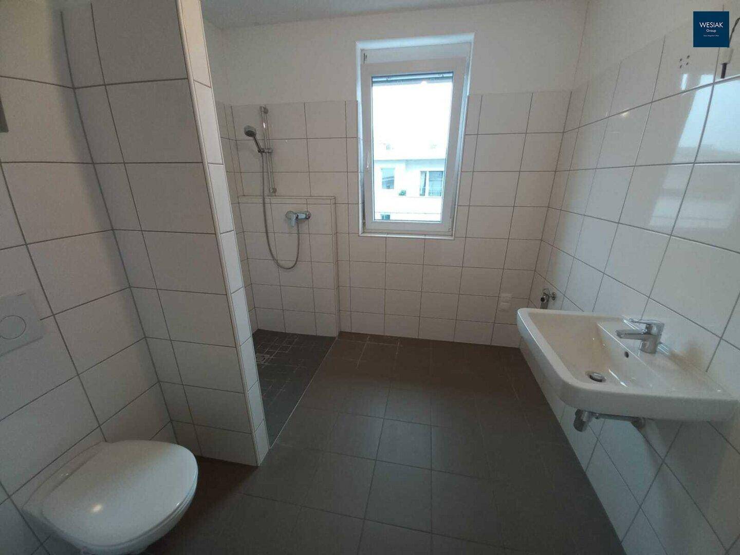 Badezimmer mit Dusche, WC, Waschbecken und Fenster, hell gefliest und funktional.
