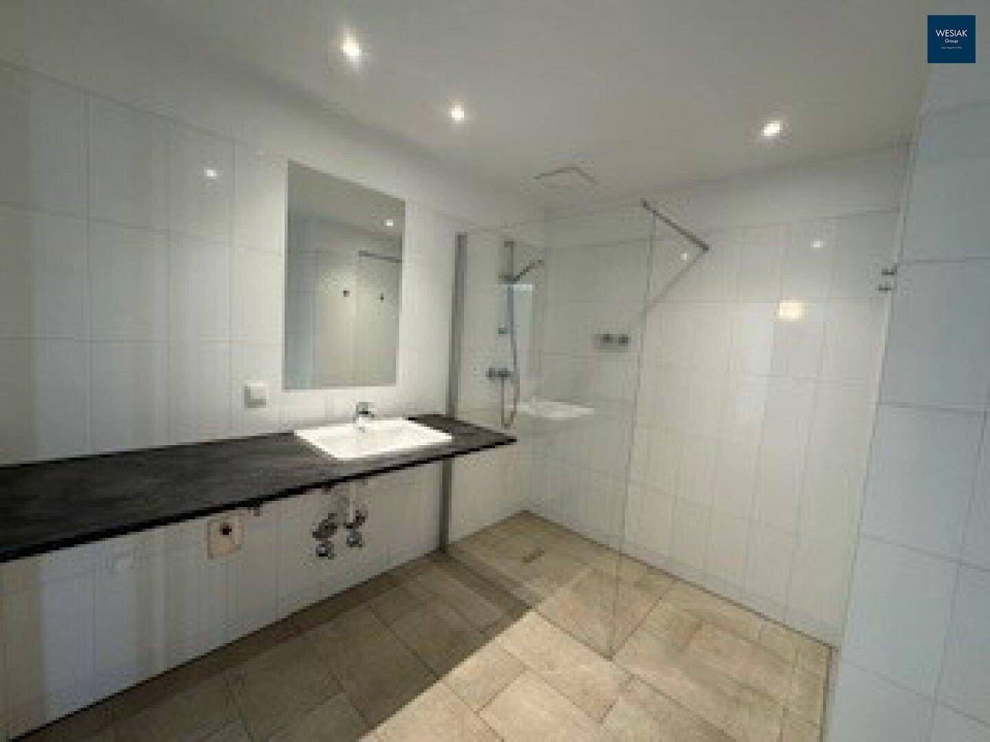 Modernes Badezimmer mit weißen Fliesen, großem Waschbecken und einer begehbaren Dusche.