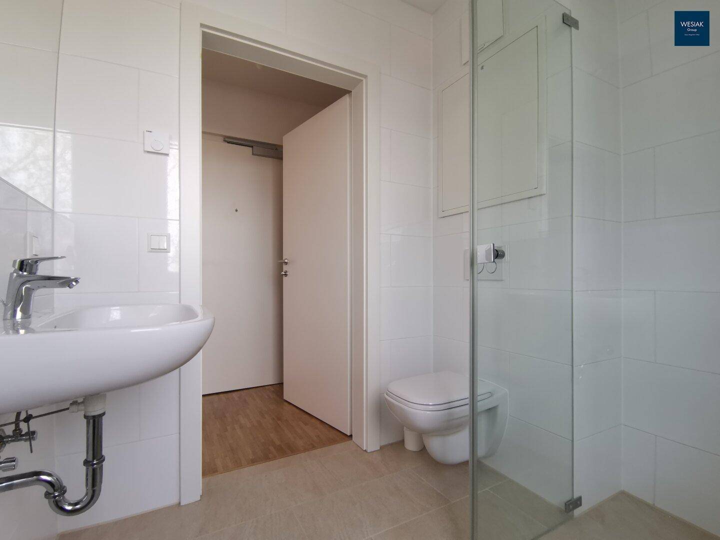Modernes Badezimmer mit weißen Fliesen, wandhängendem WC und Duschkabine.