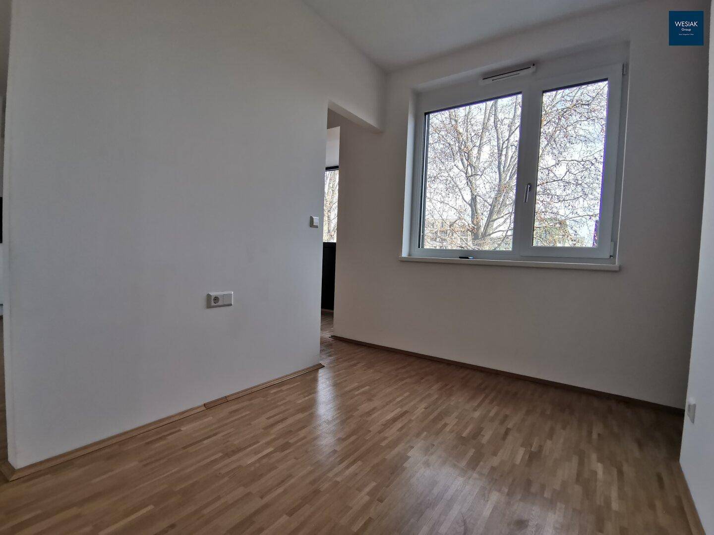 Heller Raum mit Parkettboden und einem Fenster, das viel Tageslicht hereinlässt.