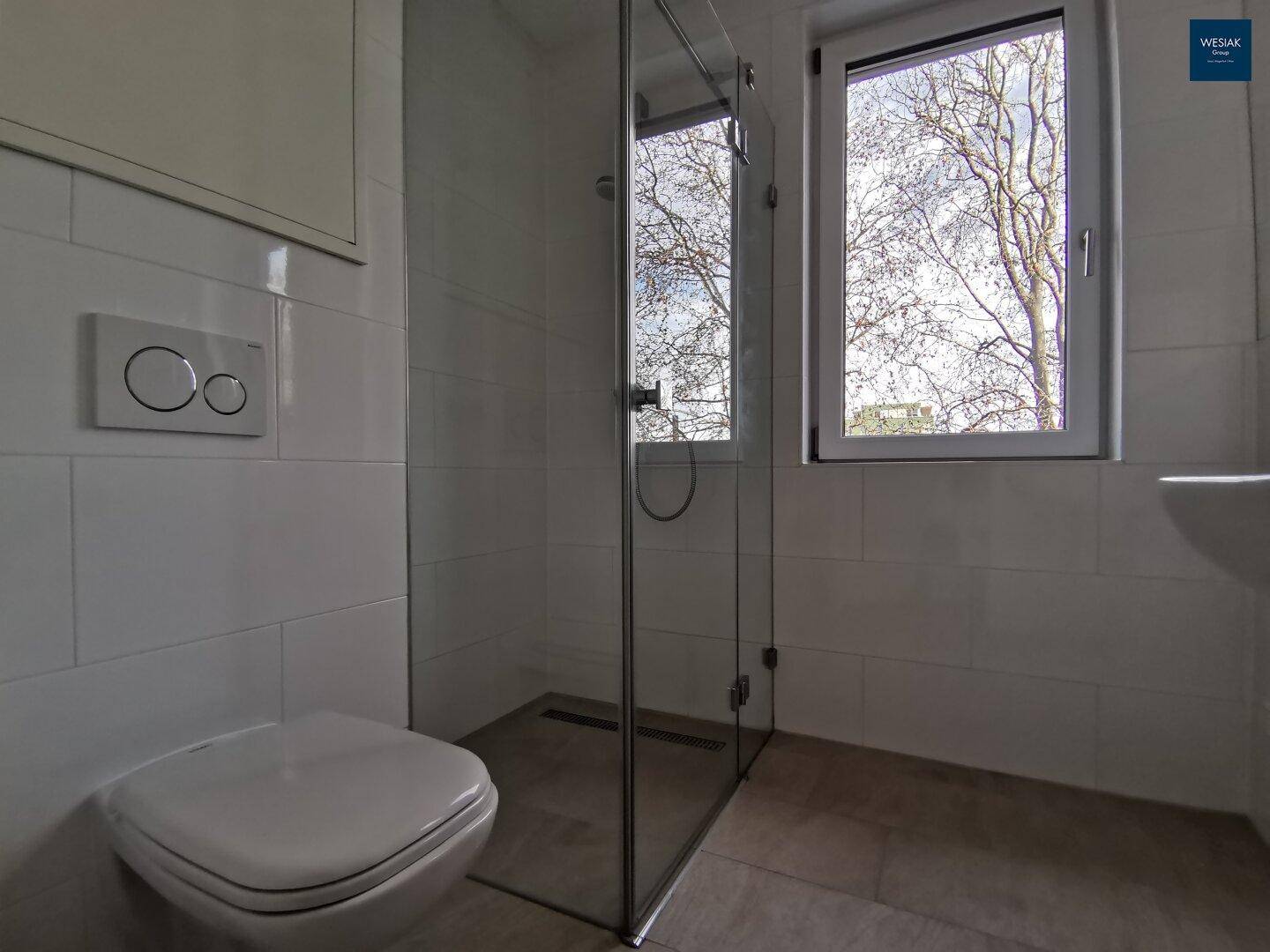 Helles Badezimmer mit Fenster, Duschkabine und wandhängendem WC.