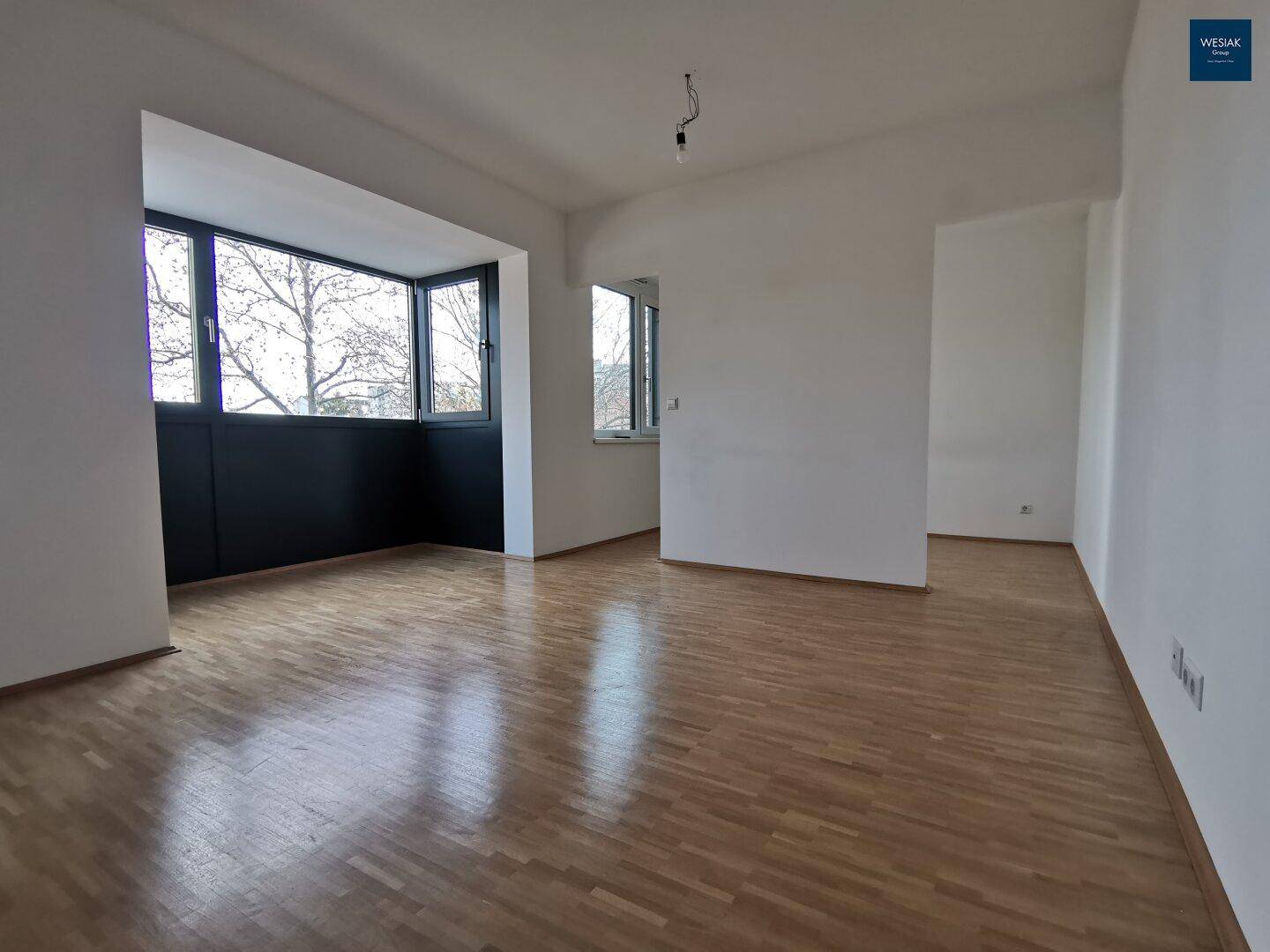 Geräumiger, leerer Wohnbereich mit Parkettboden und großen Fenstern, bereit zur Einrichtung.