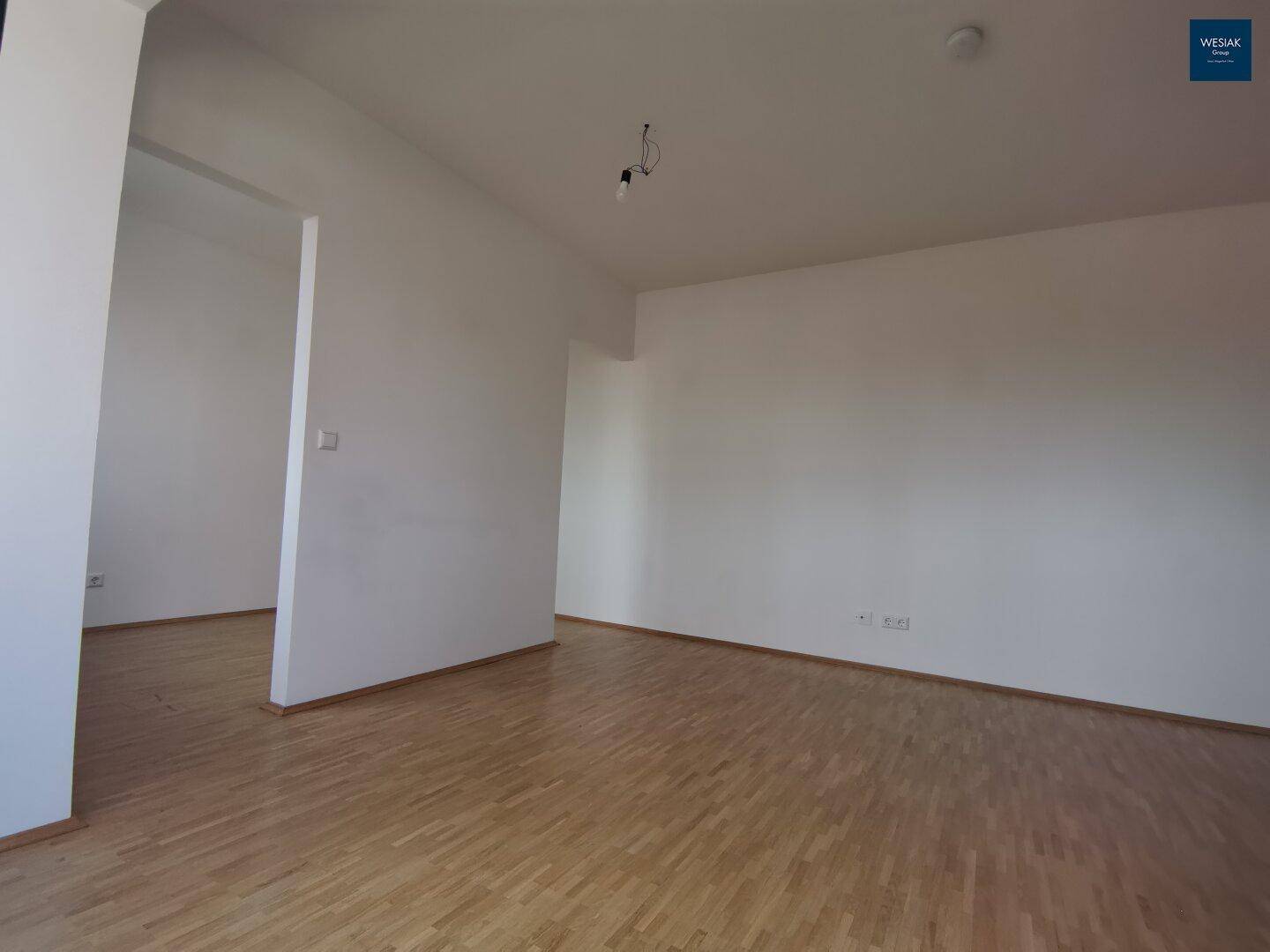 Großer, heller Wohnbereich mit Parkettboden und weißen Wänden, ideal für individuelle Gestaltung.