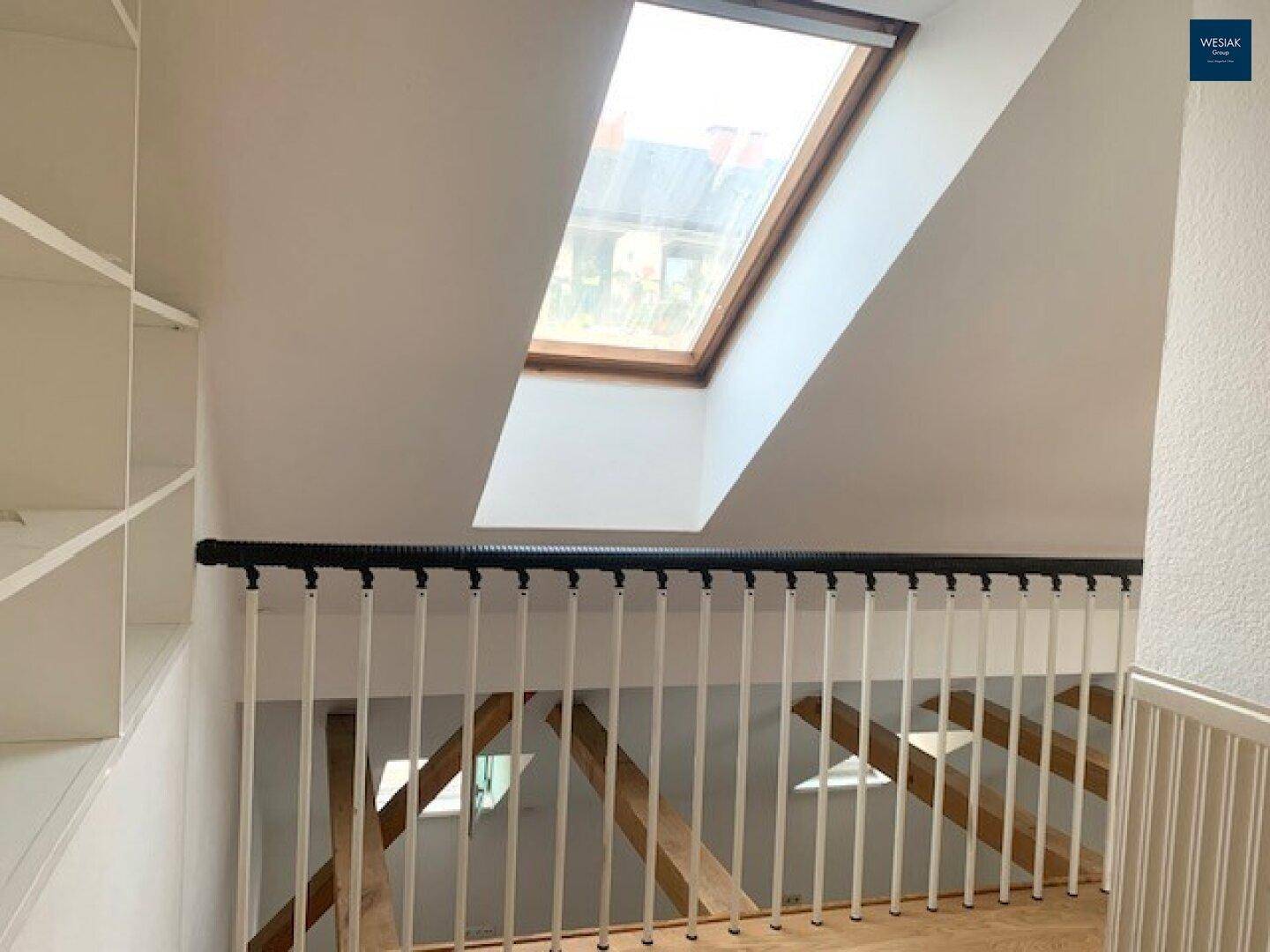 Heller Flurbereich im Dachgeschoss mit Treppengeländer, Dachfenster und Einbauregal.