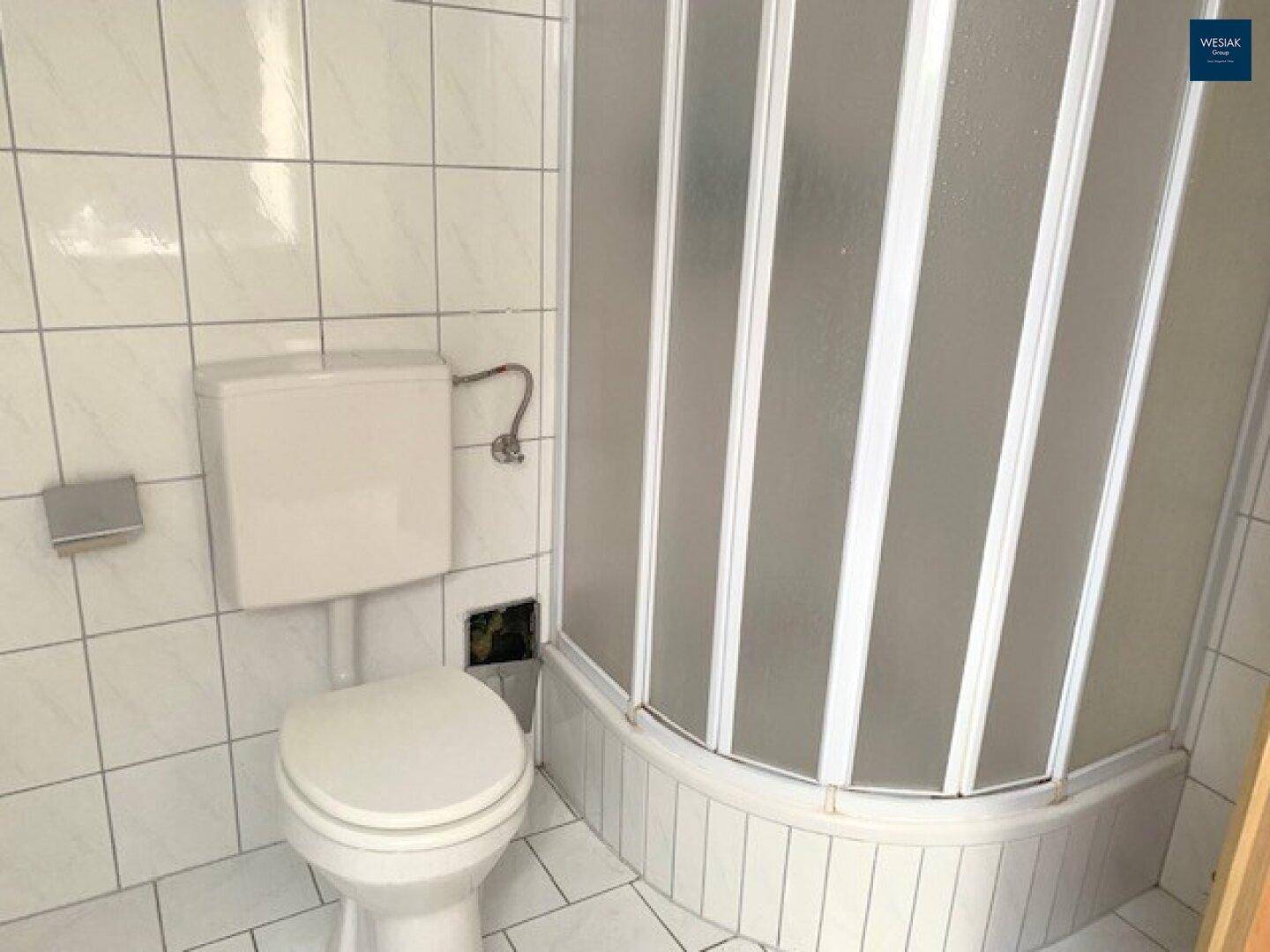 Badezimmer mit Duschkabine, WC und weißen Fliesen im klassischen Stil.