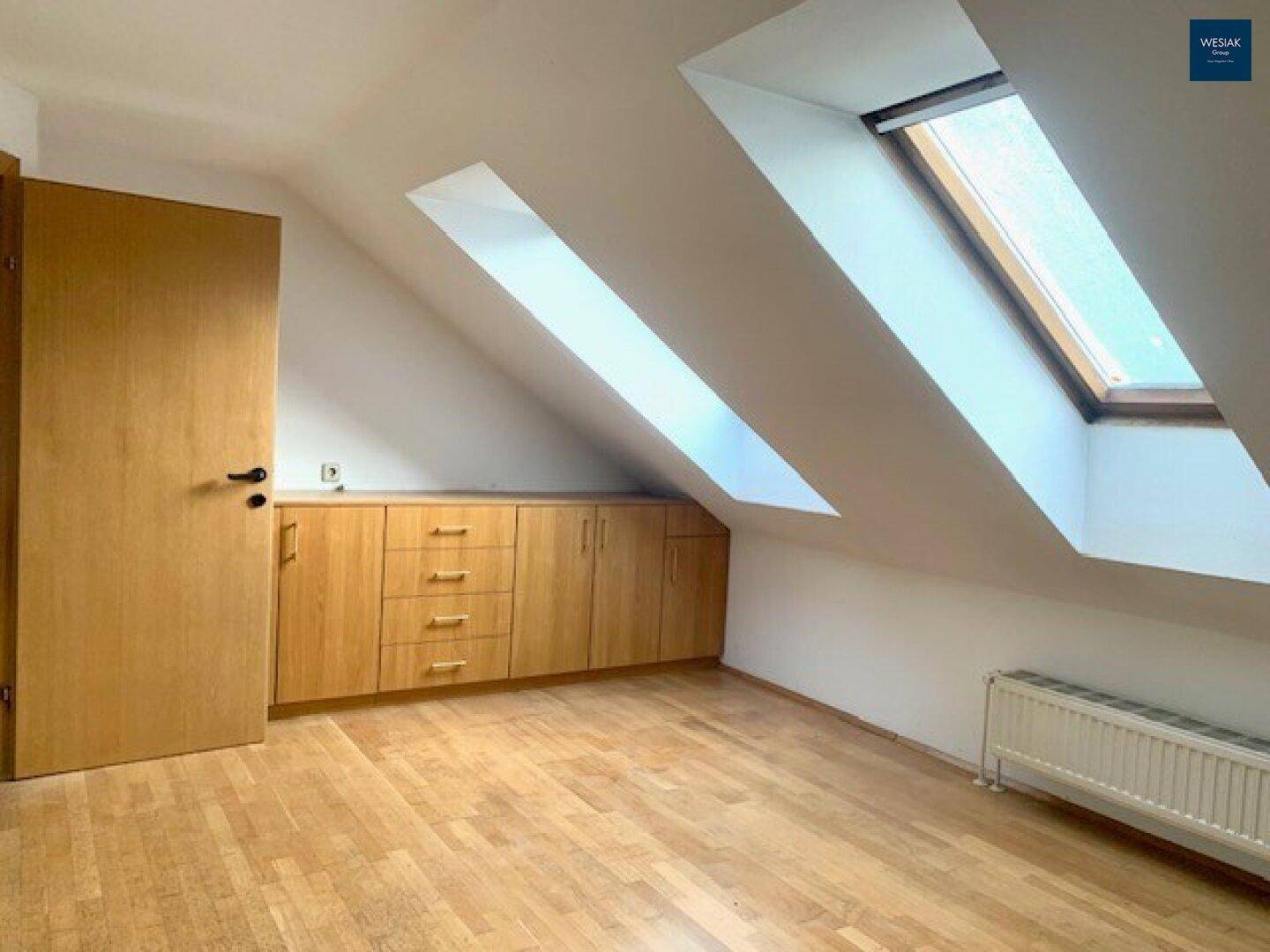 Helles Zimmer im Dachgeschoss mit Holzfußboden, Einbauschränken und Dachfenstern.