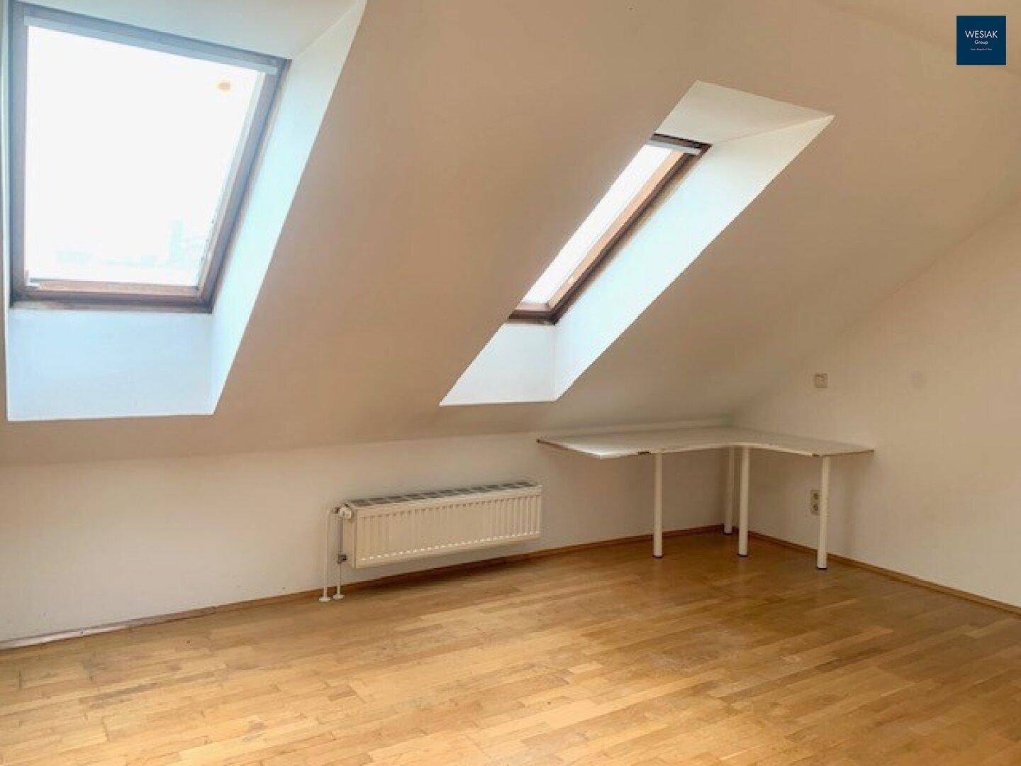 Helles Dachzimmer mit Holzfußboden, Dachfenstern und einem integrierten Schreibtisch.