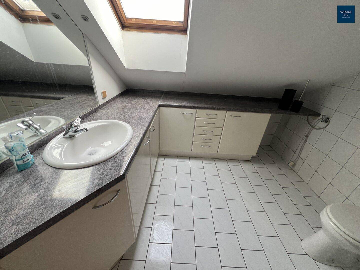 Badezimmer im Dachgeschoss mit Waschbecken, Spiegelfläche, WC und Dachfenster.