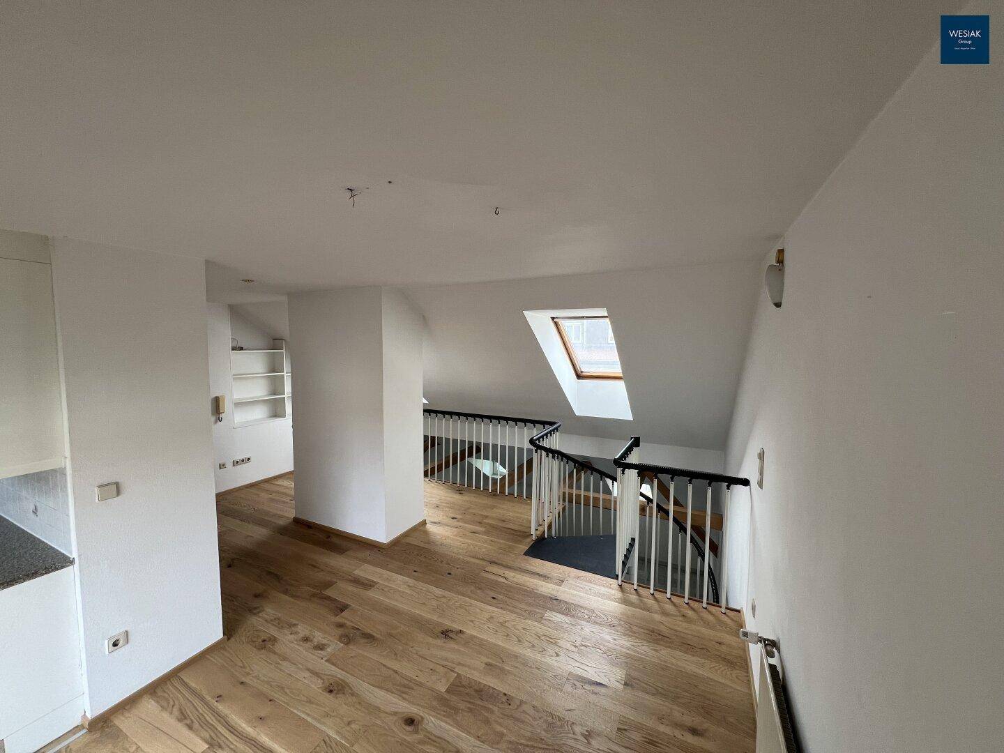 Heller Flurbereich im Dachgeschoss mit Holzfußboden, Treppengeländer und Dachfenster.