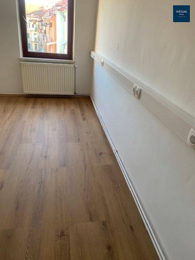 Detailansicht des Holzfußbodens und der Wand mit Fenster in einem hellen Raum.