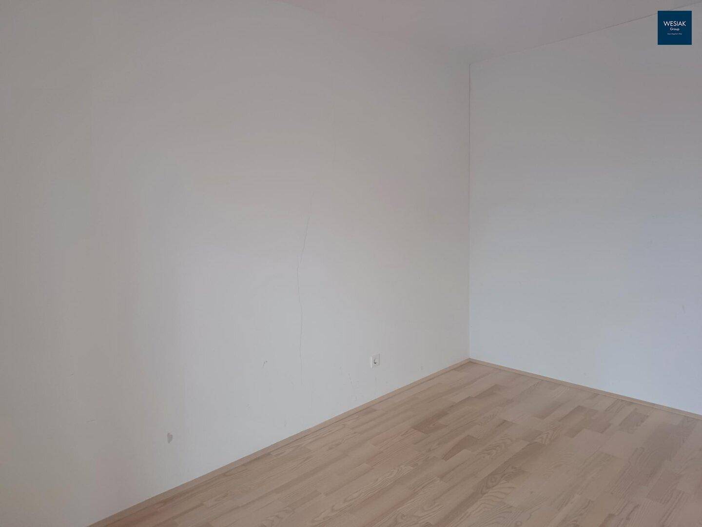 Leerer Innenraum mit weißen Wänden und hellem Holzboden, bereit für die Einrichtung.
