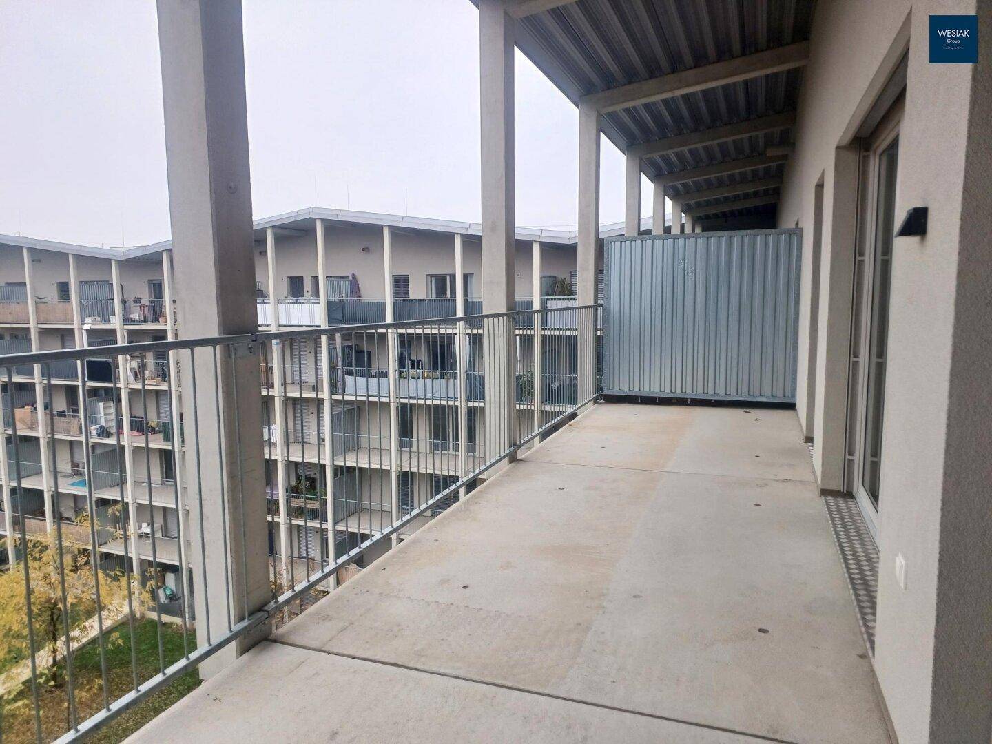Langer Balkon mit Blick auf die umliegenden Wohngebäude und die bergige Landschaft im Hintergrund.