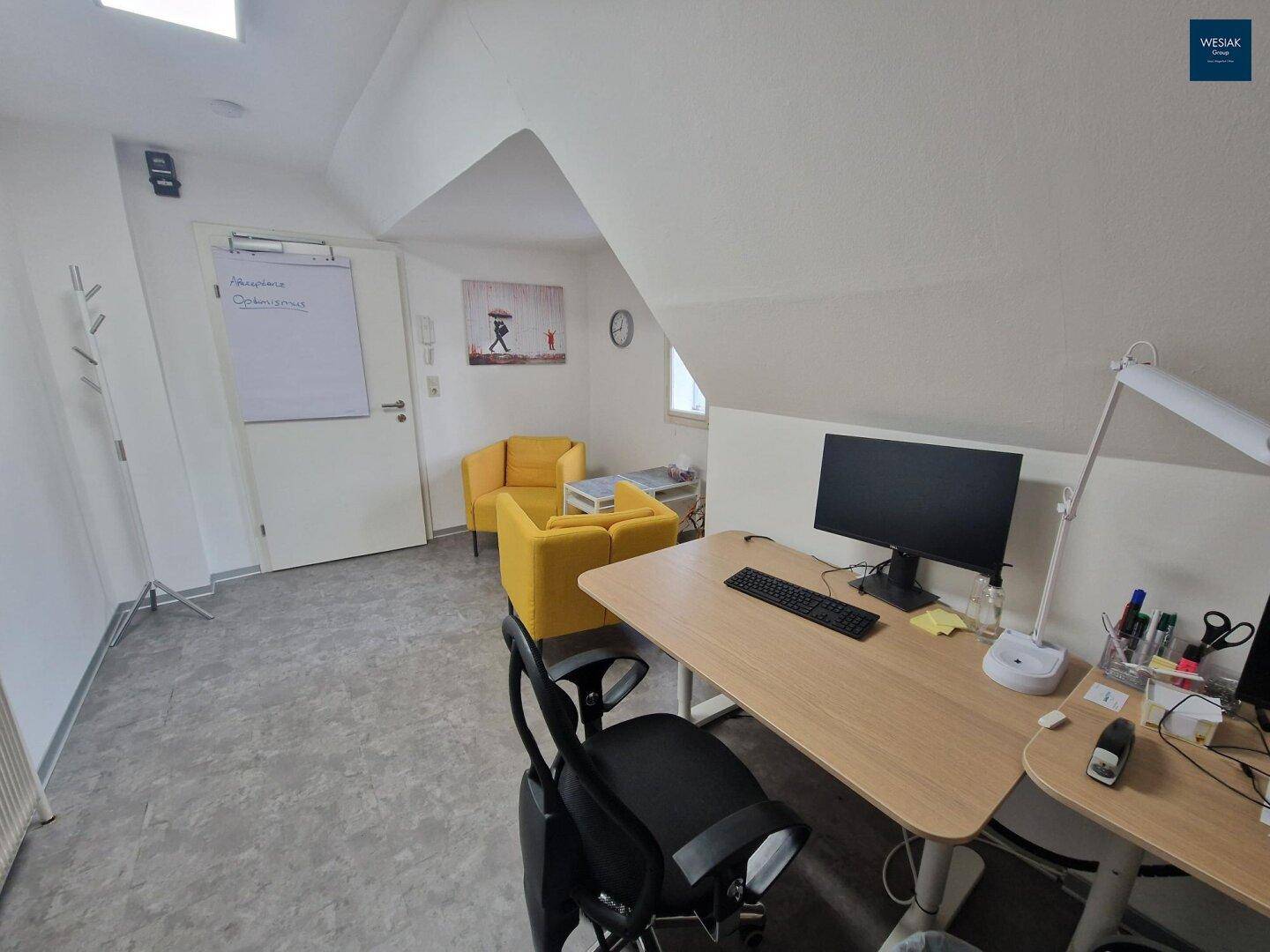 Modernes Büro mit Schreibtisch, Computer und einer gemütlichen Sitzecke unter einer Dachschräge mit Fliesenboden.