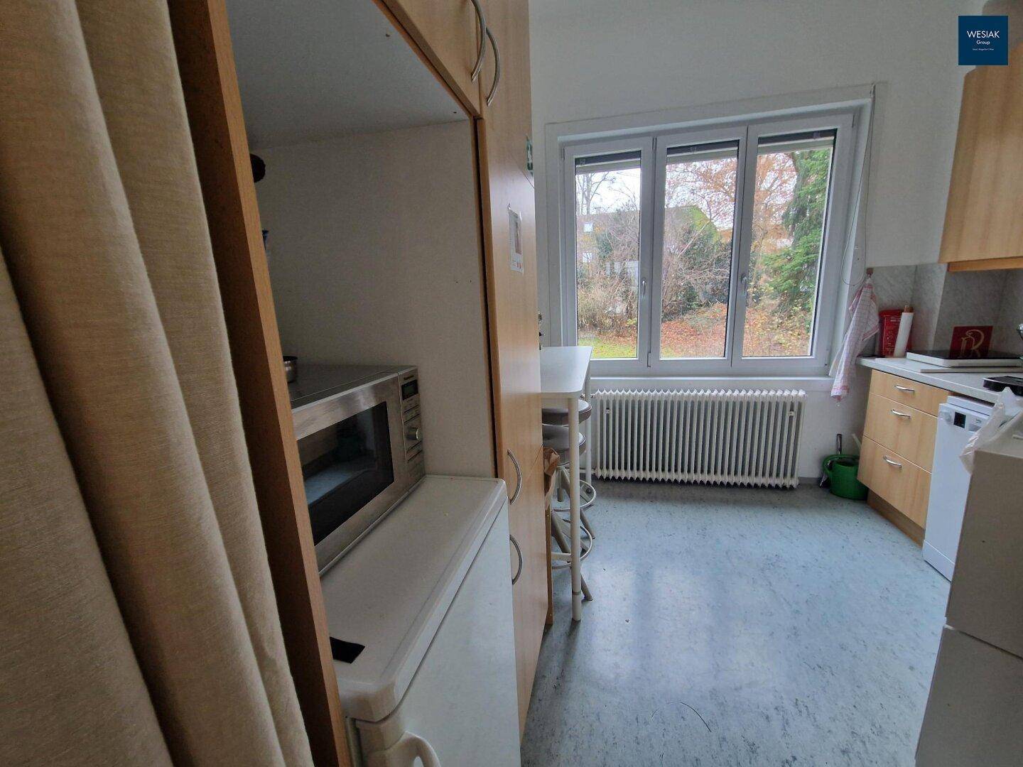 Kleine Küche mit Mikrowelle, Kühlschrank und Fenster mit Blick ins Grüne.