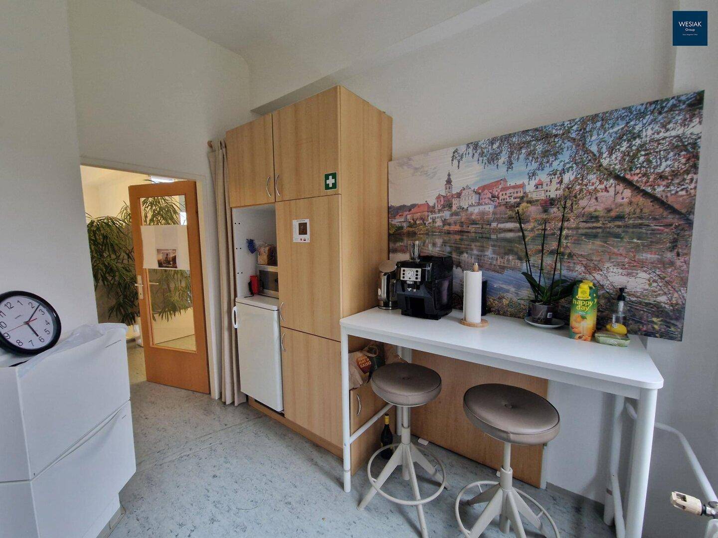 Kleine Küche mit Kaffeemaschine, Barhocker und integrierten Schränken.