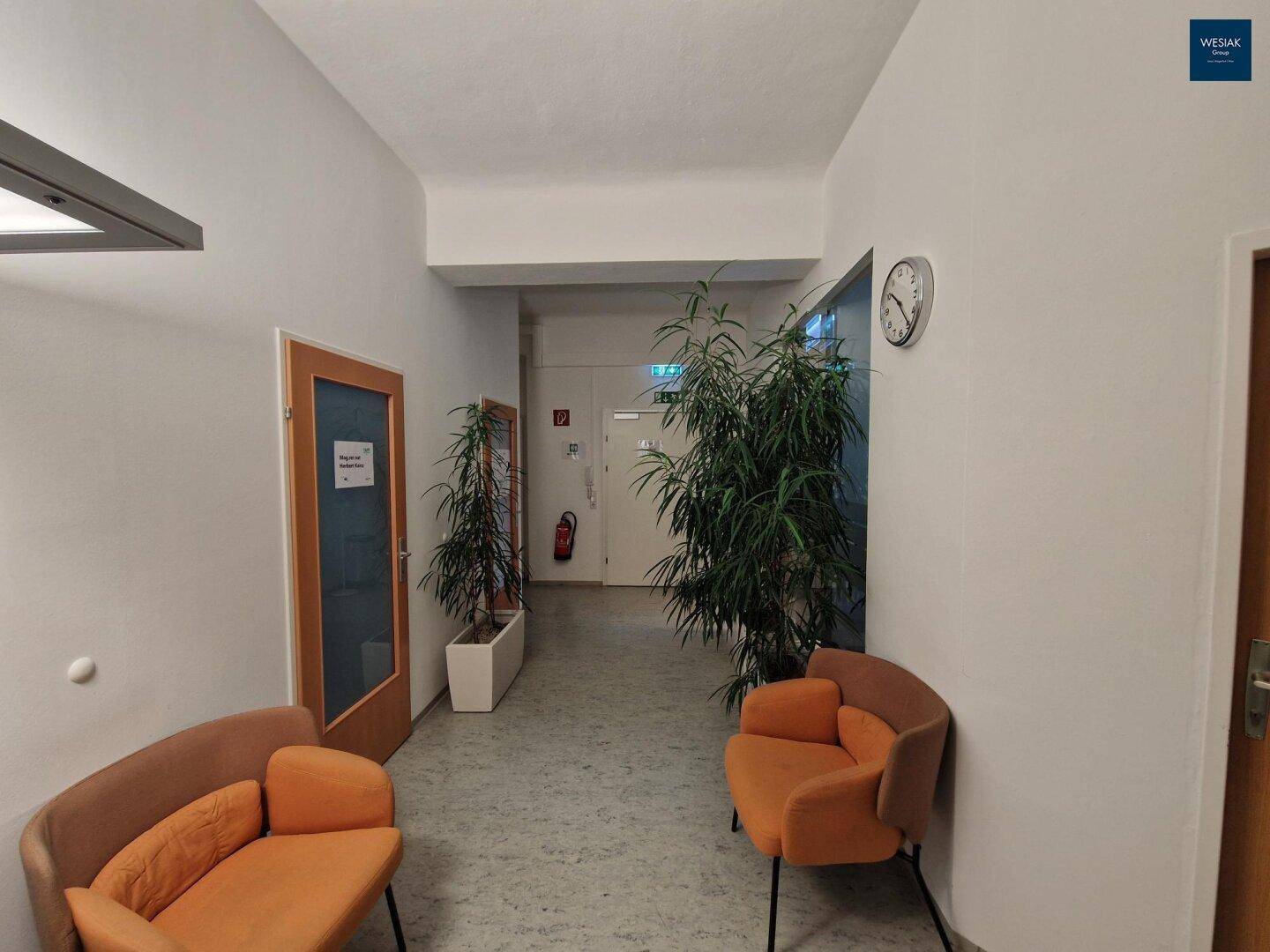 Heller Flur mit bequemen orangefarbenen Sitzgelegenheiten und großen Grünpflanzen.