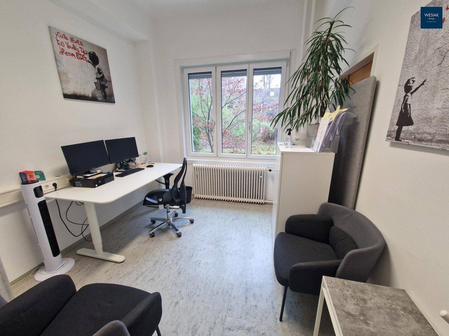 Helles Büro mit Schreibtisch, zwei Monitoren, bequemen Sesseln und Blick ins Grüne.