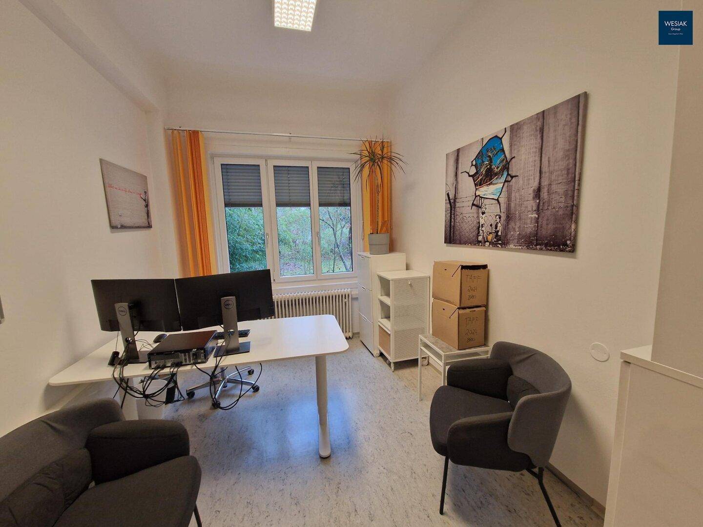 Modernes Büro mit Schreibtisch, zwei Monitoren und Blick auf Bäume.