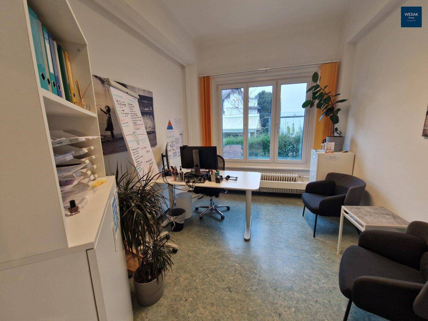 Helles Büro mit Schreibtisch, Bürostuhl, bequemen Sesseln und Blick ins Grüne.