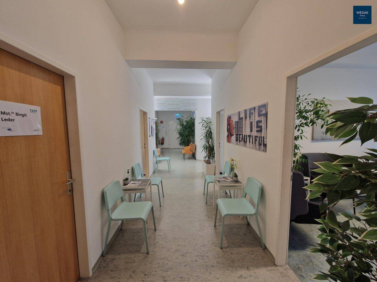 Langer, heller Flur mit mehreren Sitzbereichen und dekorativen Pflanzen.