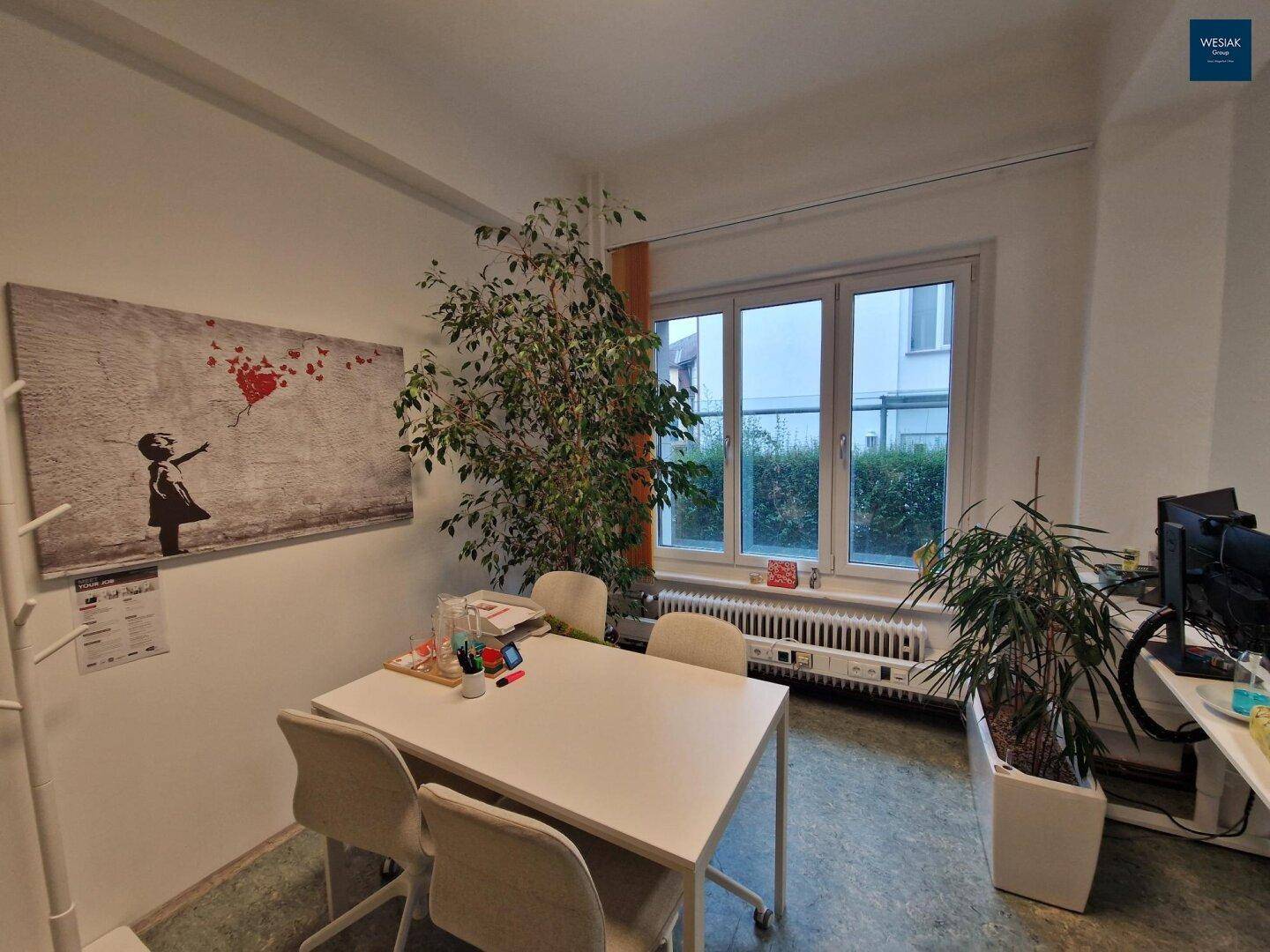 Heller Bürobereich mit kleinem Besprechungstisch, Stühlen und Pflanzen.