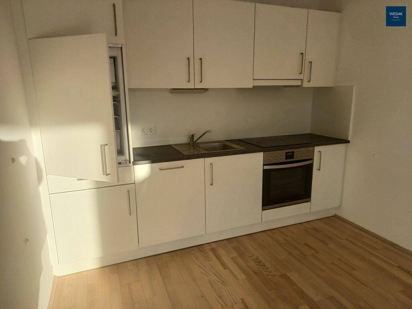 Funktionale, weiße Küchenzeile mit integrierten Geräten und hellem Holzfußboden.